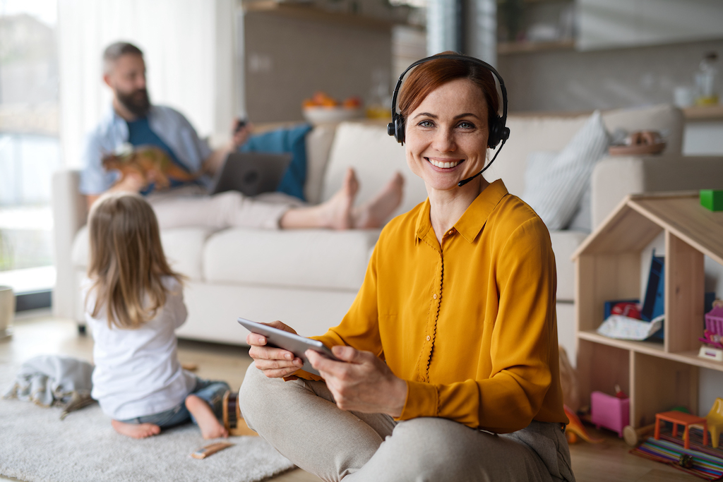 Businesswoman with tablet and headset enjoying a good work life balance working indoors at home, everyday with child