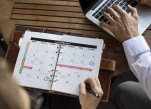 Woman with personal organizer organising schedule alongside man with laptop