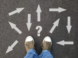 image of feet standing on asphalt with multitude of arrows pointing in different directions and a question mark, for a confusion, choice , uncertainty concept